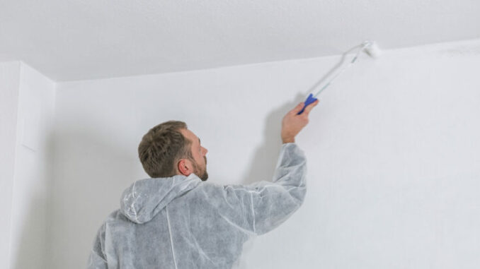 young painter working with paint roller to paint the ceiling of a room with white color. do it yourself concept image